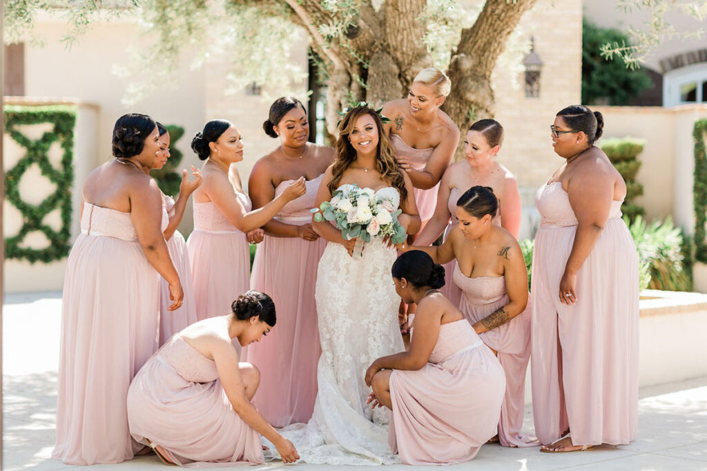 Bridesmaids in pale pink hues surround bride at rustic wedding.