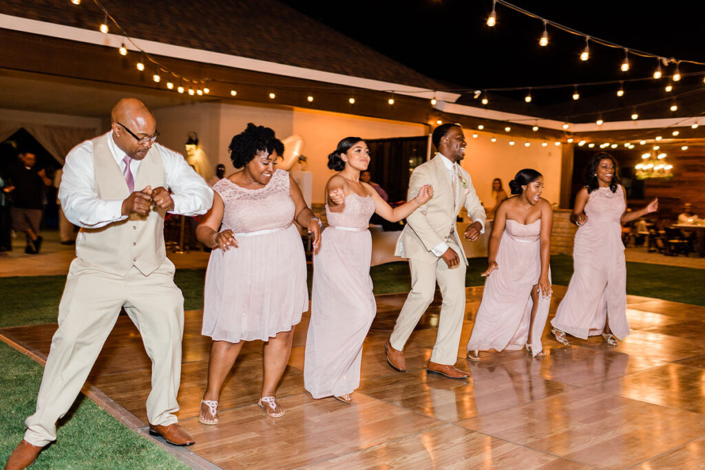 Groom and family on the dance floor perform for his bride at rustic wedding.