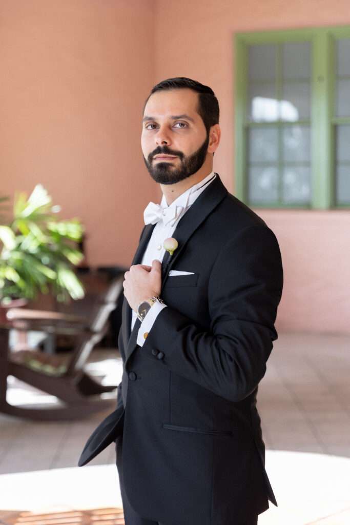 Groom poses in classy black tux before classic luxurious wedding ensues.